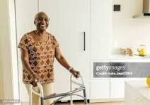 Smiling elderly woman using a walker for support indoors.